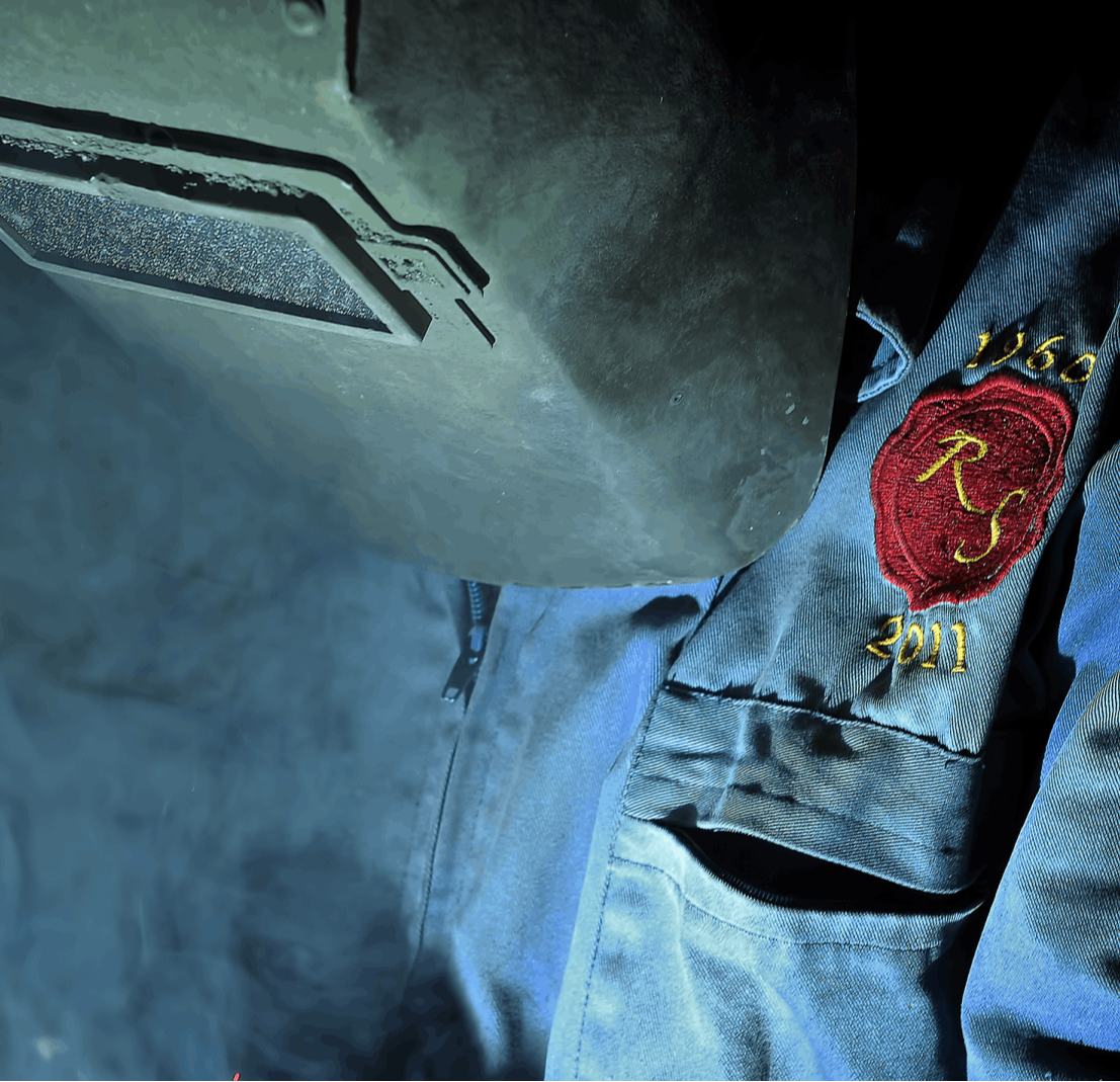 Detalle de un trabajador soldando con equipo de protección, resaltando el uniforme con bordado personalizado de Rubber Seal y la precisión en el proceso de fabricación metálica.